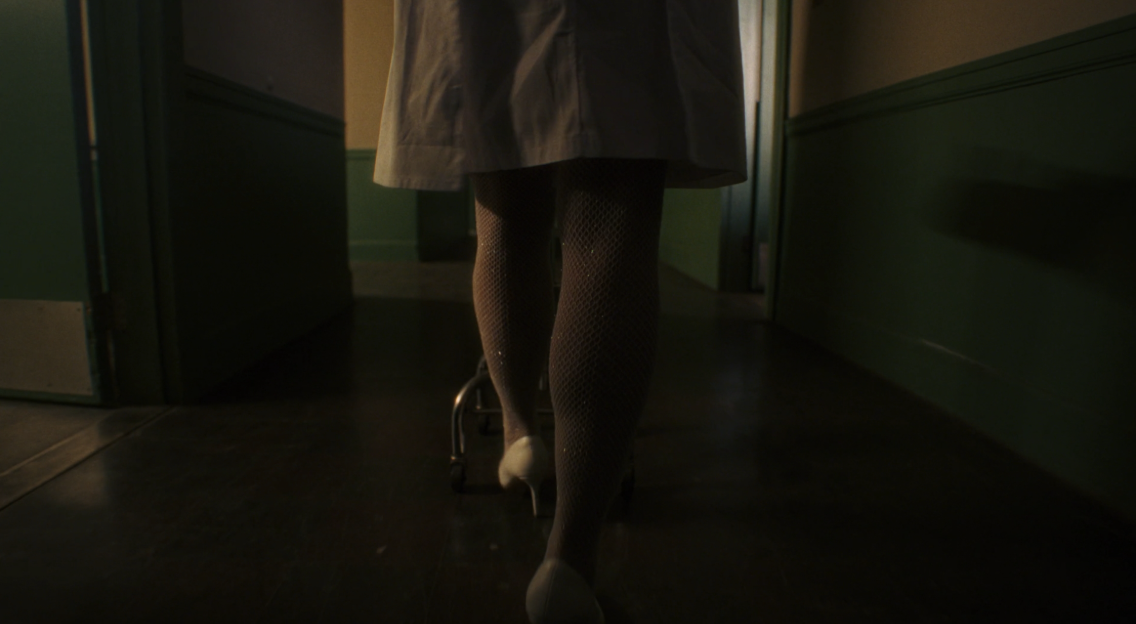 A figure walking away down a dim institutional hallway